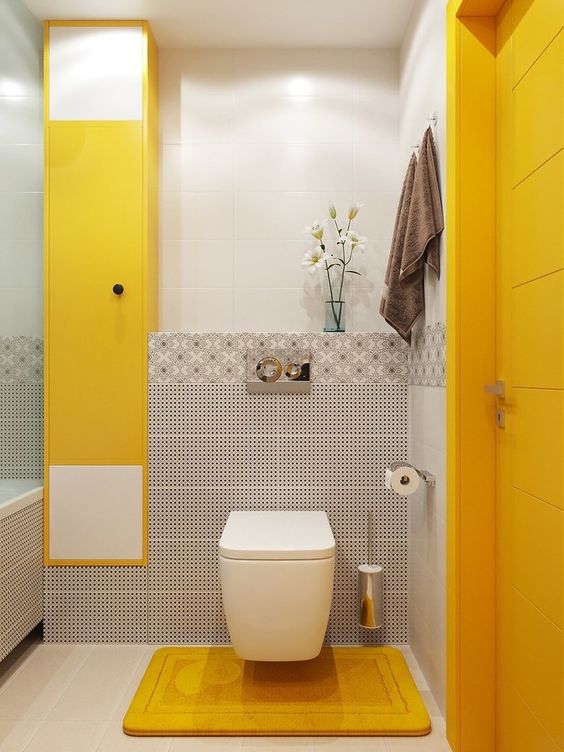 a bright bathroom with white, grey tiles, bold yellow panels, a yellow door and a yellow rug on the floor