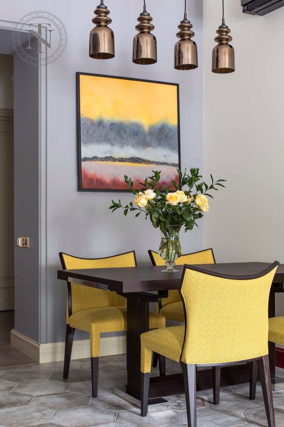 a chic and bright dining space with a grey and lavender wall, a dark table, bright yellow chairs, a colorful artwork and pendant lamps