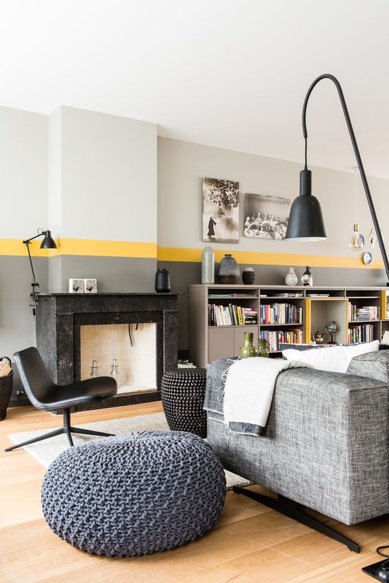 a chic living room with a grey and yellow color block wall, a grey sofa, a black tile fireplace and black furniture