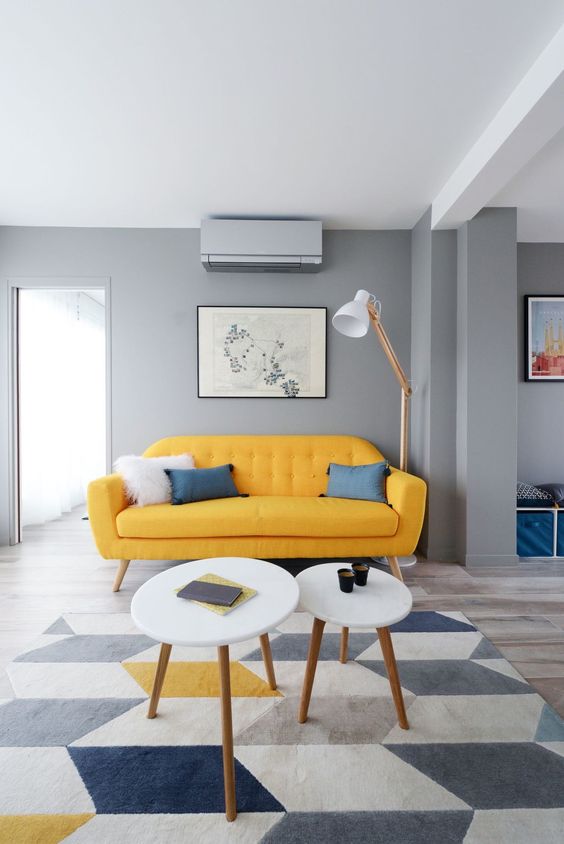 a cool mid century modern living room with grey walls, a yellow sofa, round tables, a floor lamp and a geo rug