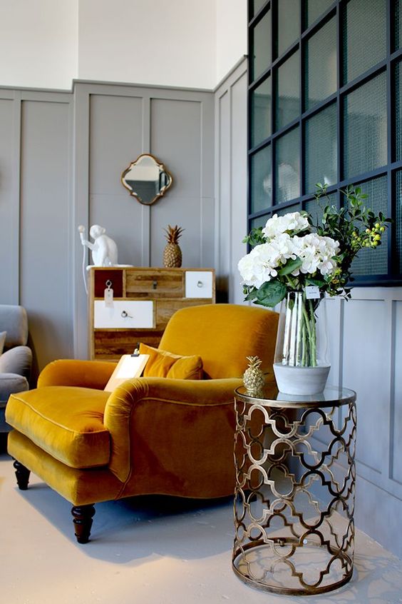 a dove grey paneled nook with a honey yellow vintage chair, a wooden cabinet, a gold coffee table and gold touches