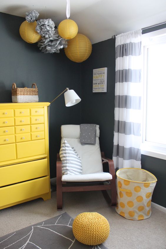 a graphite grey nursery with a bold dresser, a lounger, bright yellow paper lamps and an ottoman plus striped curtains