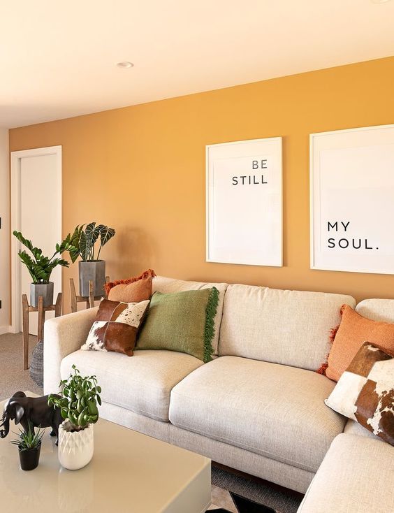 a modern living room with yellow walls, neutral furniture, printed pillows, potted greenery and some cool prints