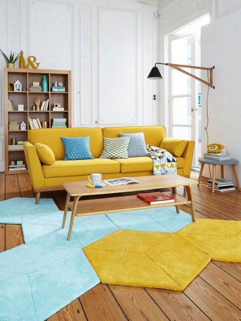 a pretty mid century modern living room with a yellow sofa, a geometric blue and yellow rug, an open storage unit and a wall sconce