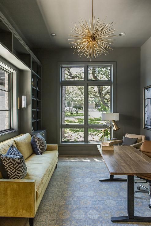 a refined home office with grey walls, built in storage units, a yellow sofa, leather chairs, a desk and gold touches
