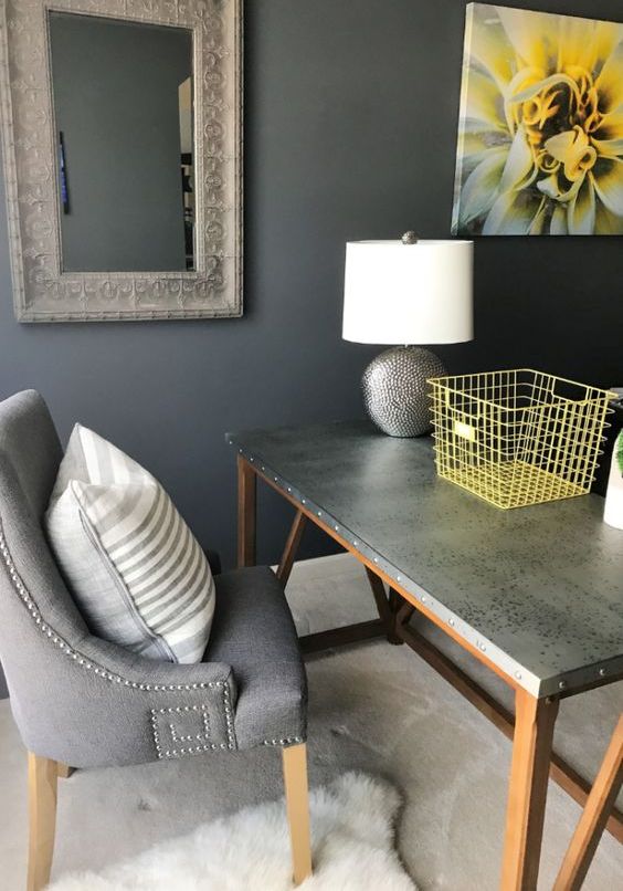 a small home office nook with grey walls, a grey desk and a chair, a pretty lamp with a grey base and some yellow accessories