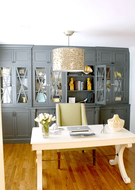 a stylish vintage home office with a grey storage unit that takes a whole wall, a vintage desk, a lemon yellow chair and a metallic pendant lamp