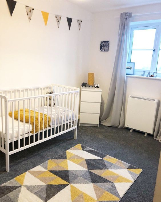 a white nursery with a grey floor, a geometric rug, white furniture, grey and mustard bedding, a matching banner and grey curtains