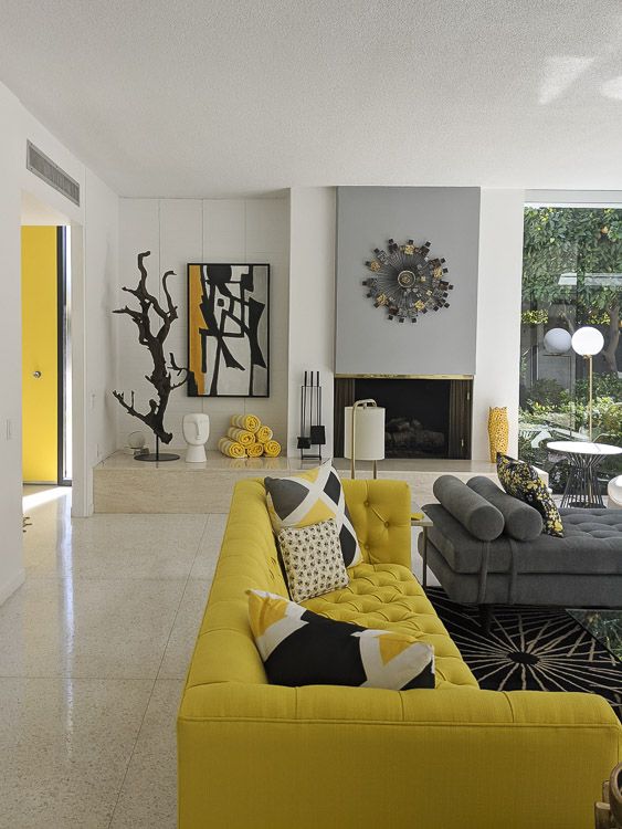 an elegant living room with a grey and yellow furniture, a fireplace, printed rugs and pillows and a pretty artwork