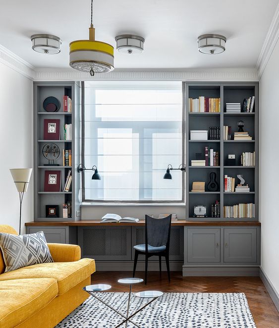 an elegant vintage home office with a built in grey storage unit, a vintage chair, a yellow sofa, a coffee table trio and a pendant lamp