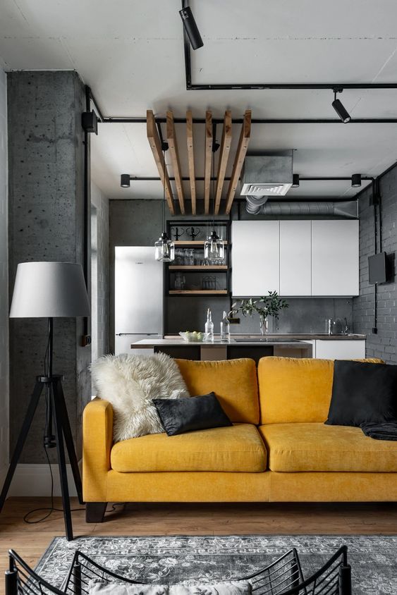 an industrial grey space with white cabinetry, black exposed pipes and a bold accent - a honey yellow sofa that makes a statement