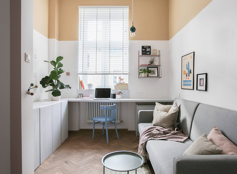 The living room features a sofa, a table and a comfy windowsill working space, color block walls make the room catchy and cheerful
