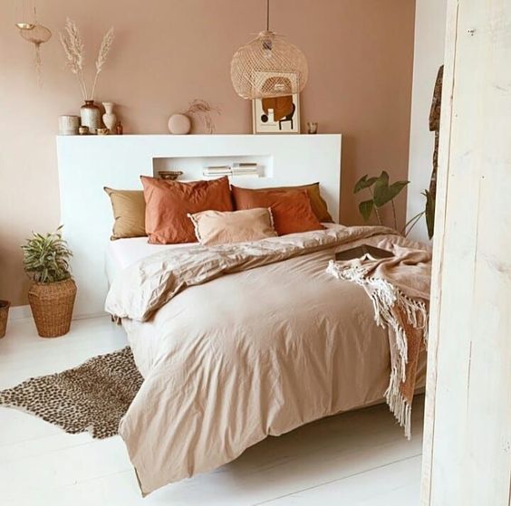 a contemporary boho earthy bedroom with a terracotta wall, earthy tone bedding, vases, artworks and a pendant lamp