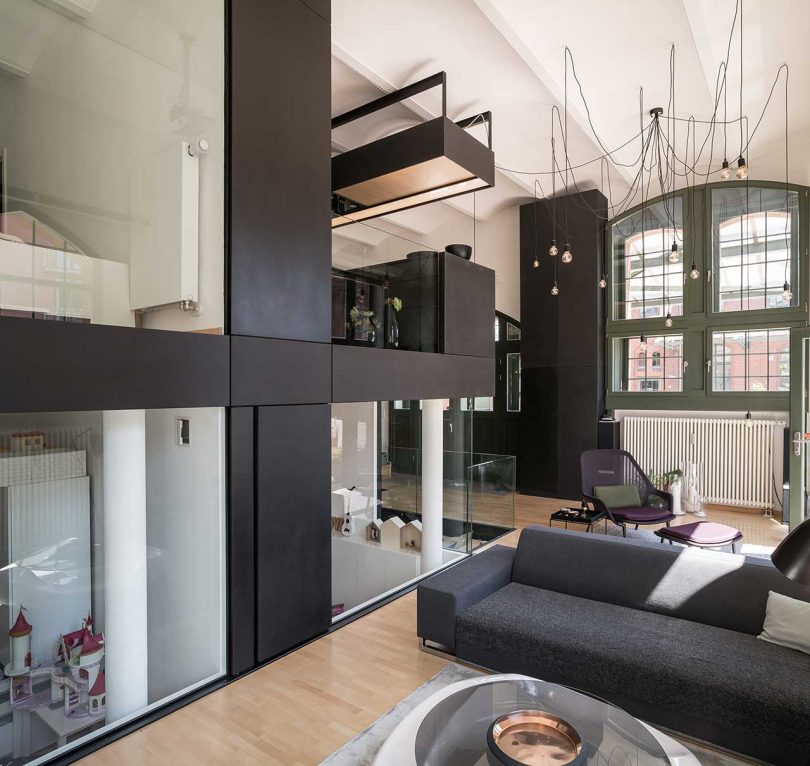 The living room shows off a laconic grey sofa, a glass coffee table and a catchy and comfy reading chair in purple with a footrest The living room shows off a laconic grey sofa, a glass coffee table and a catchy and comfy reading chair in purple with a footrest