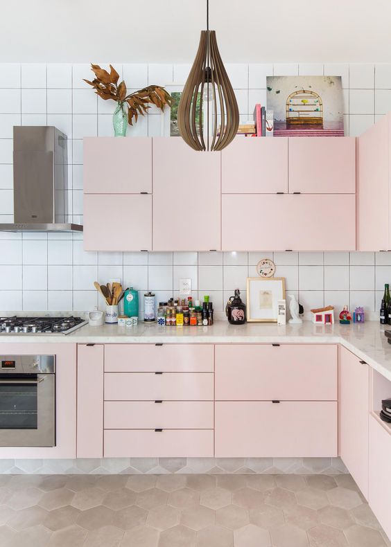 a modern pastel kitchen done in soft pink, with a catchy pendant lamp and a white square tile backsplash
