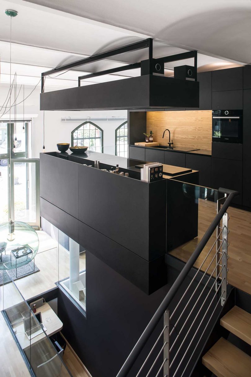 The kitchen upstairs is a super minimalist space done with sleek black cabinetry, with a light-colored wooden backsplash and a kitchen island that makes it more comfortable to use