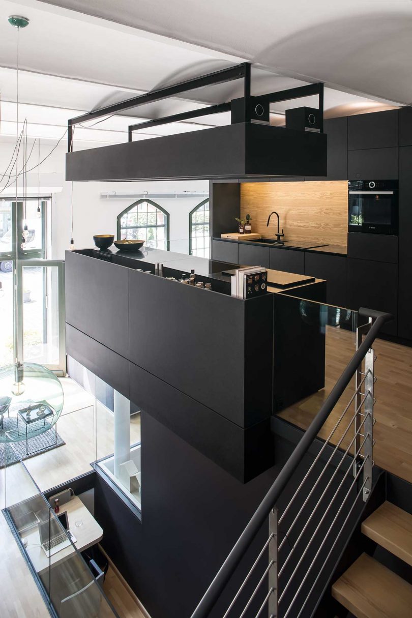 The kitchen upstairs is a super minimalist space done with sleek black cabinetry, with a light colored wooden backsplash and a kitchen island that makes it more comfortable to use The kitchen upstairs is a super minimalist space done with sleek black cabinetry, with a light-colored wooden backsplash and a kitchen island that makes it more comfortable to use
