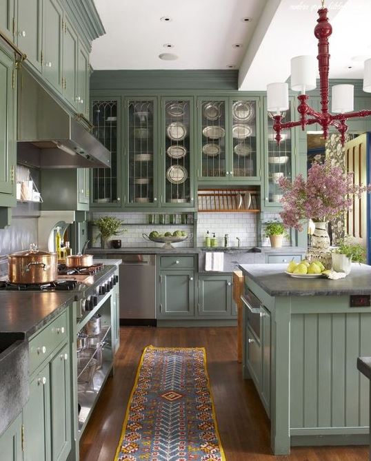 a vintage sage green kitchen with glass and usual cabinets, grey stone counterops, a white tile backsplash and a vintage chandelier