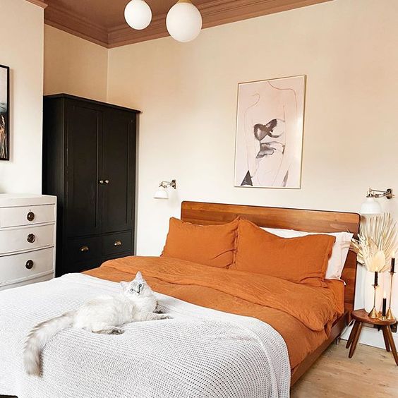 a chic modern bedroom with black and white furniture, a rich stained bed, orange bedding, leaves and grasses