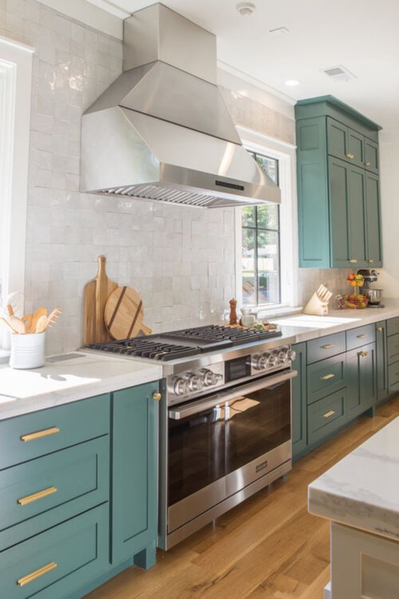 a beautiful teal kitchen with white stone countertops and a white tile backsplash and touches of gold looks bold