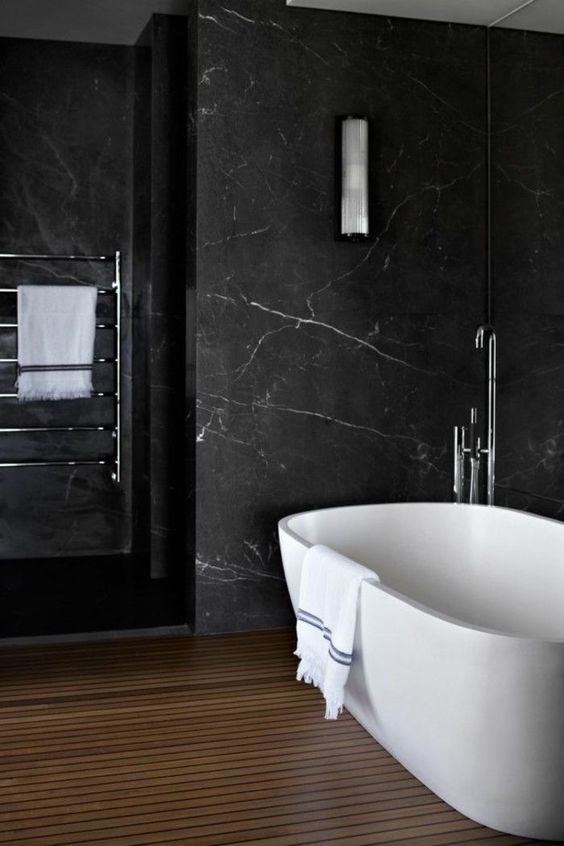 a refined bathroom with black marble walls, a wooden slab floor, a pretty tub and neutral fixtures