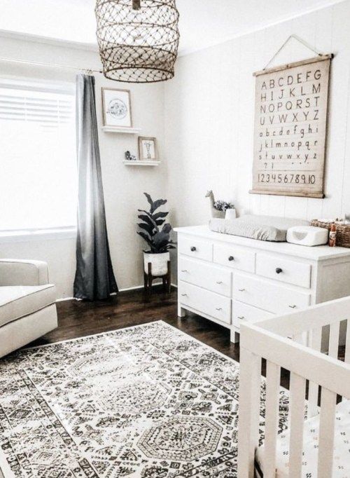 a gender neutral nursery with white furniture, a printed rug, a simple artwork and a catchy pendant lamp
