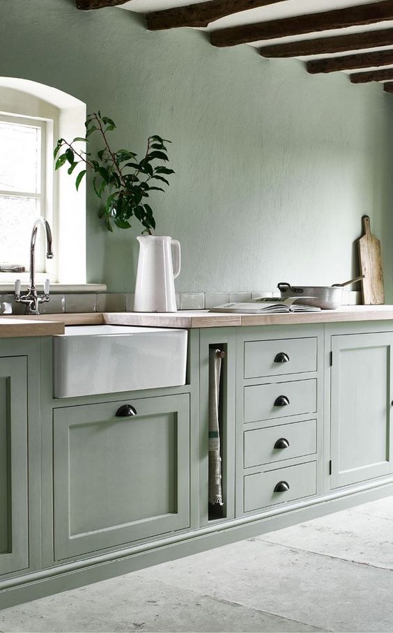 a sage green kitchen with matching walls and cabinetry, wooden beams on the ceiling and wooden countertops plus dark handles