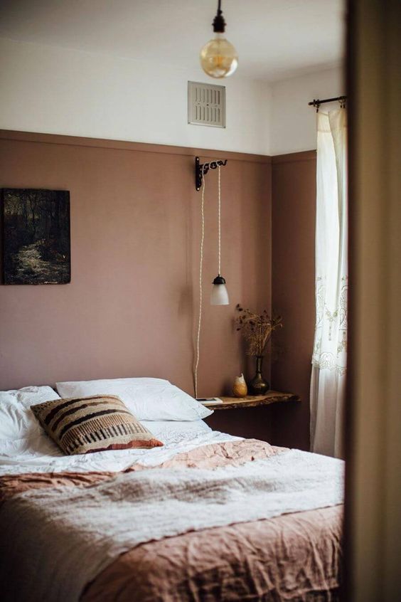 an earthy toned bedroom with a mauve statement wall, floating nightstands, terracotta bedding and simple lamps