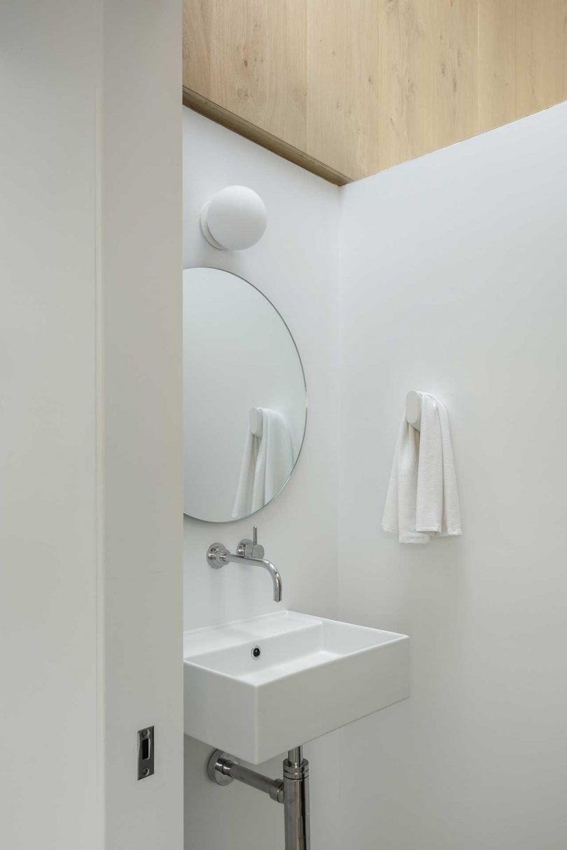 The bathroom is done neutral, with a round mirror, a sink and some lamps on the walls