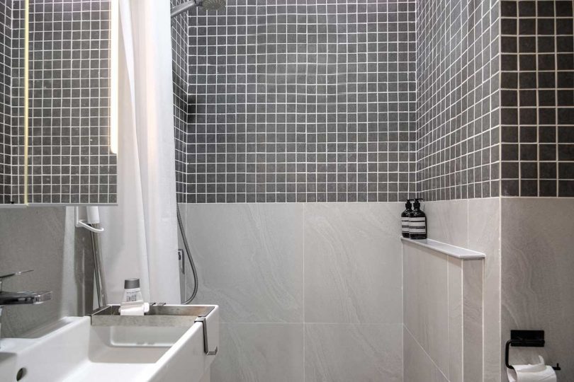 10 The bathroom is done with light and dark grey tiles, white appliances and a small shower space