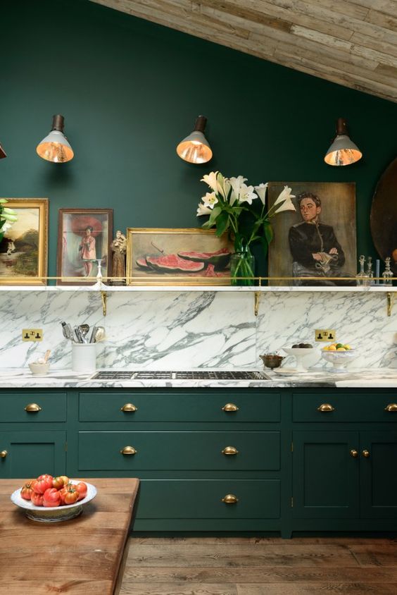 a vintage hunter green kitchen with a white marble backsplash and countertops, a shelf with artworks is chic