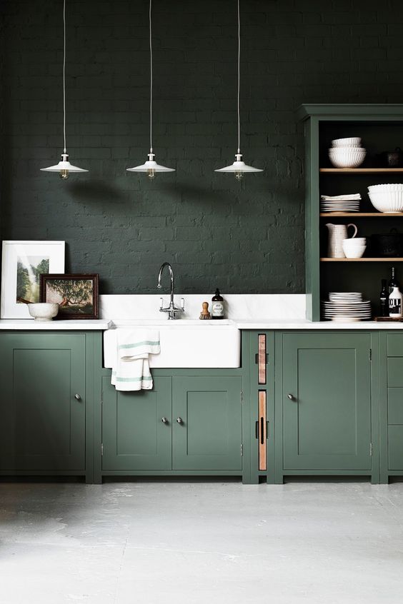 a moody hunter green kitchen with vintage cabinets, dark green brick walls, a white stone backsplash and countertops