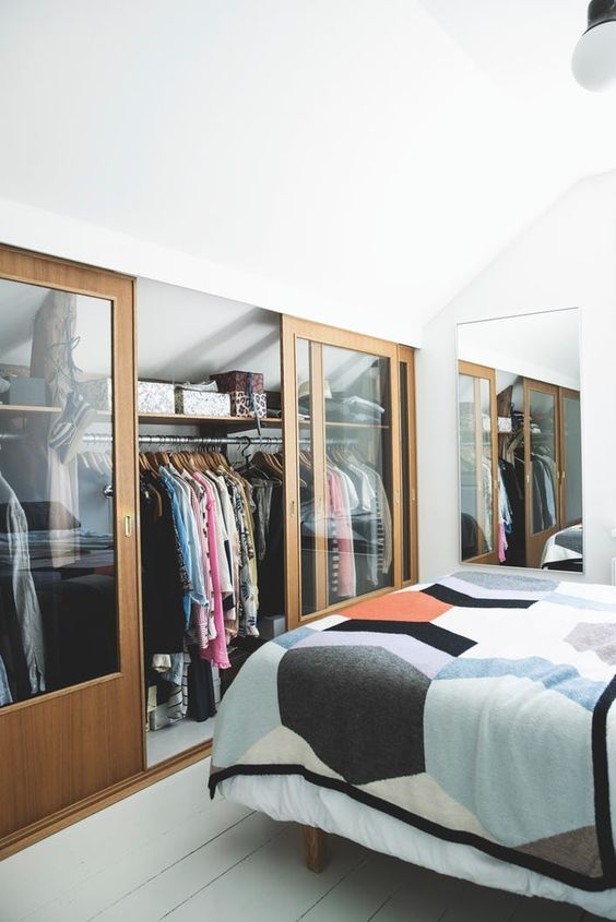 a small attic bedroom in neutrals, with its awkward part covered with sliding glass doors and used as a closet