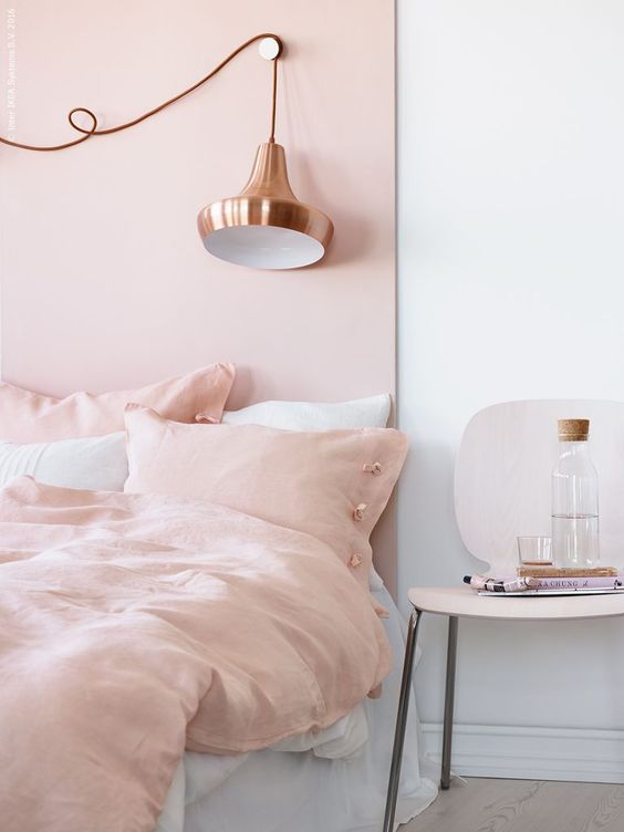 a welcoming and inviting bedroom with a blush accent wal and matching bedding plus a copper lamp