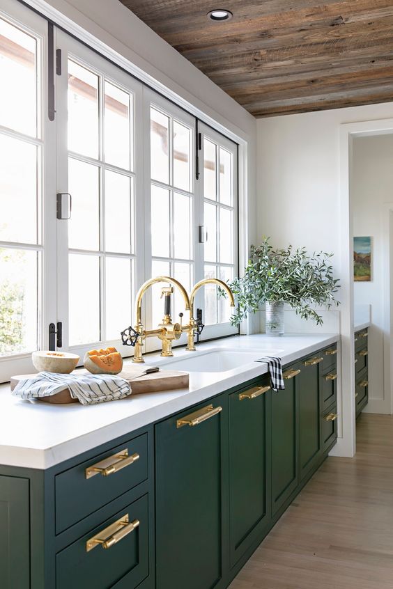 16 a hunter green modern kitchen with white stone countertops, gold handles and fixtures and a window instead of a backsplash