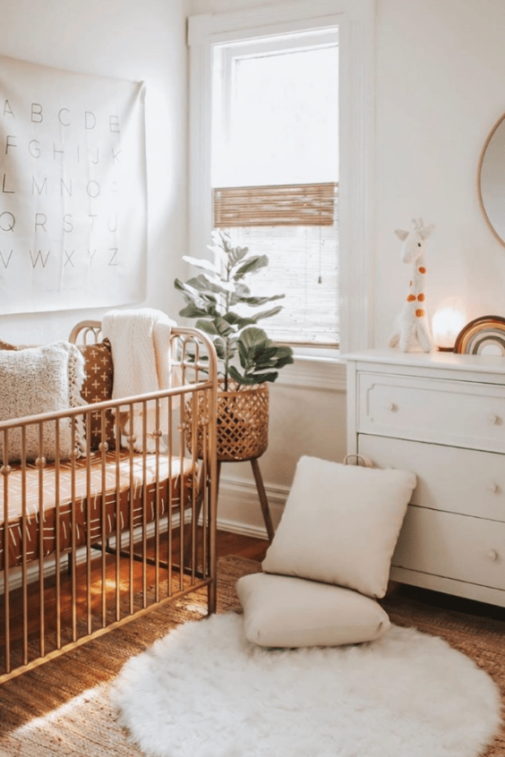 a welcoming neutral hygge nursery with a metal crib and white furniture, neutral textiles and a potted plant