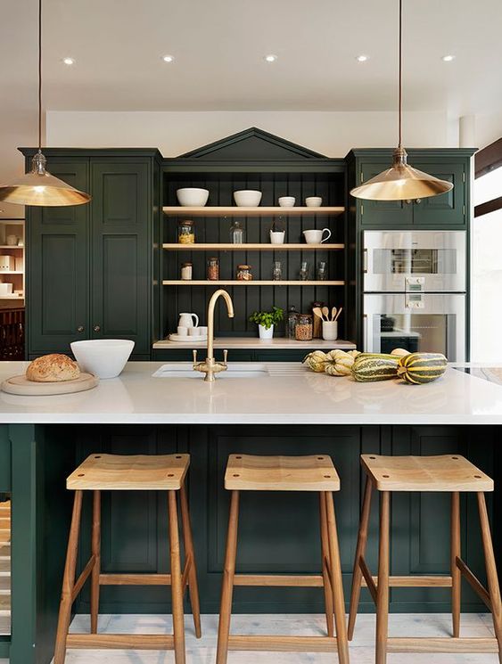 a sophisticated hunter green kitchen with vintage cabinets, open shelves, white countertops, metal pendant lamps and wooden stools