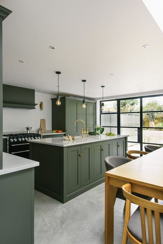 a stylish hunter green kitchen with vintage cabinetry, a white backsplash and countertops, pendant bulbs and a glazed wall