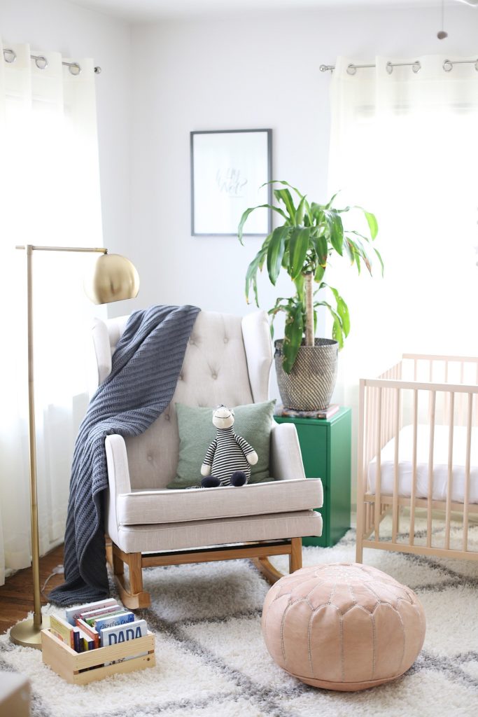 a stylish and welcoming neutral boho nursery with neutral furniture, a potted plant and a brass floor lamp