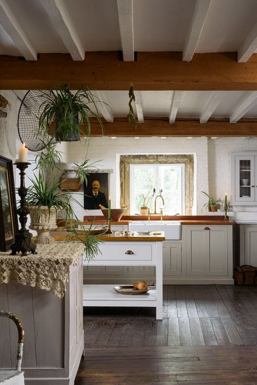 a beautiful old world kitchen with wooden beams, elegant neutral cabinets, potted greenery and candles in candleholders