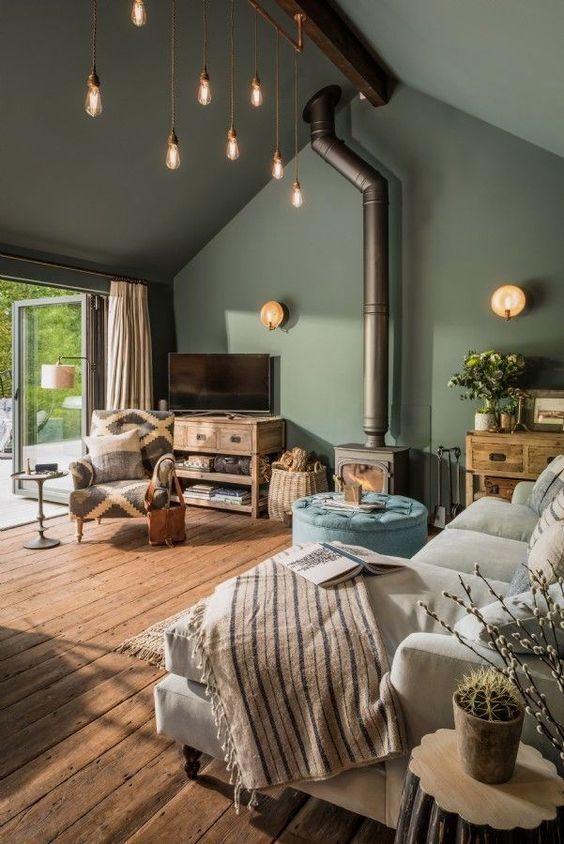a welcoming living room with green walls and a ceiling, with neutral and wooden furniture and a hearth plus bulbs hanging down