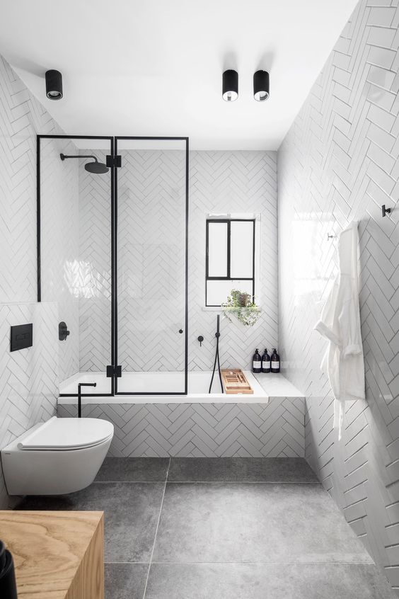 a contemporary bathroom with glossy white tiles, large scale tiles on the floor, black fixtures and a window for more light