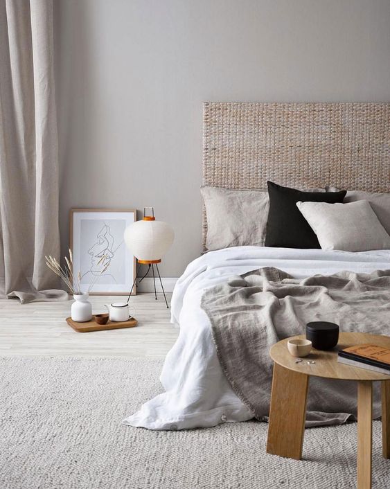 a stylish and welcoming Japandi bedroom with a rattan bed, wooden furniture, grey and white bedding and lamps