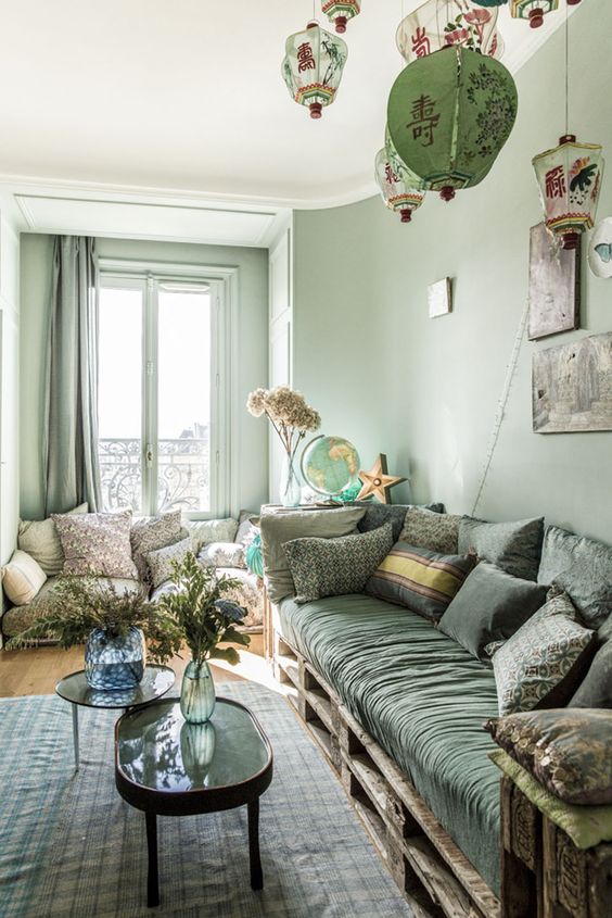 a monochromatic and eclectic green living room with light green walls, a dark green sofa, printed textiles and Asian lanterns
