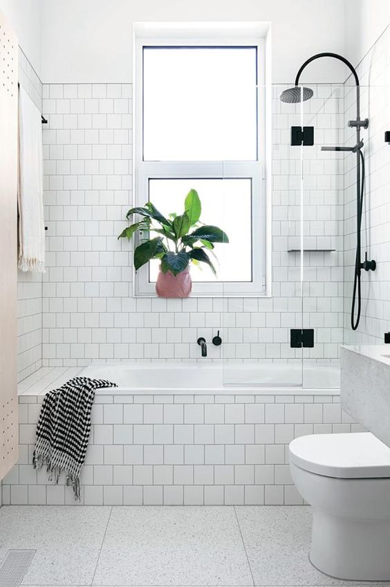 a white Scandinavian bathroom done with square tiles, a tub clad with tiles, black fixtures and a floating vanity
