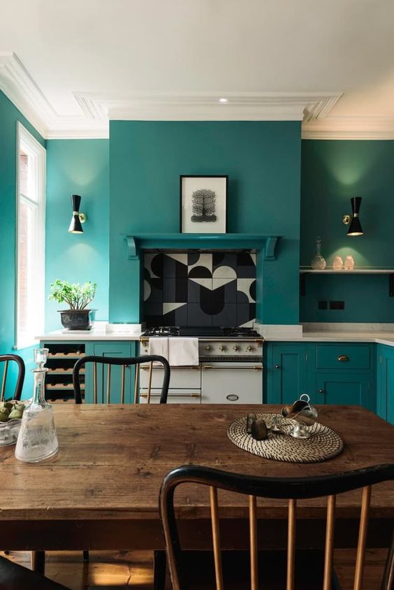 a teal kitchen with chic cabinets and matching walls for a sleek look, white stone countertops and a dining zone with vintage furniture