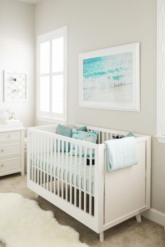 an ocean-inspired nursery with turquoise, blue and white, with a pretty artwork and lovely printed bedding