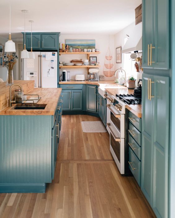 a stylish farmhouse kitchen in teal, with butcherblock countertops, a white backsplash and gold fixtures