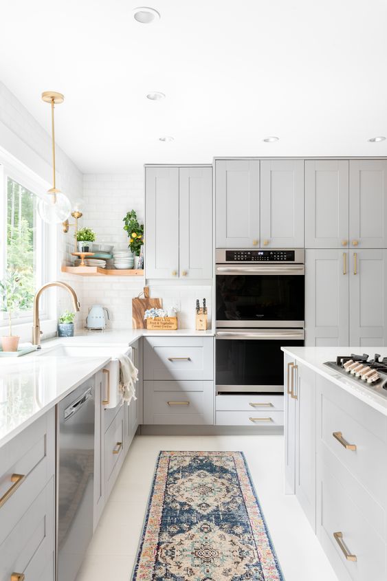 a gorgeous dove grey kitchen with white stone countertops and a tile backsplash, gold fixtures and handles