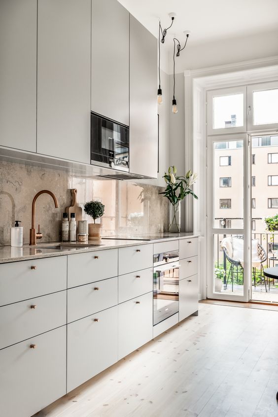 a stylish contemporary kitchen with sleek cabinets, thiny knobs, a tan stone backsplash and bulbs